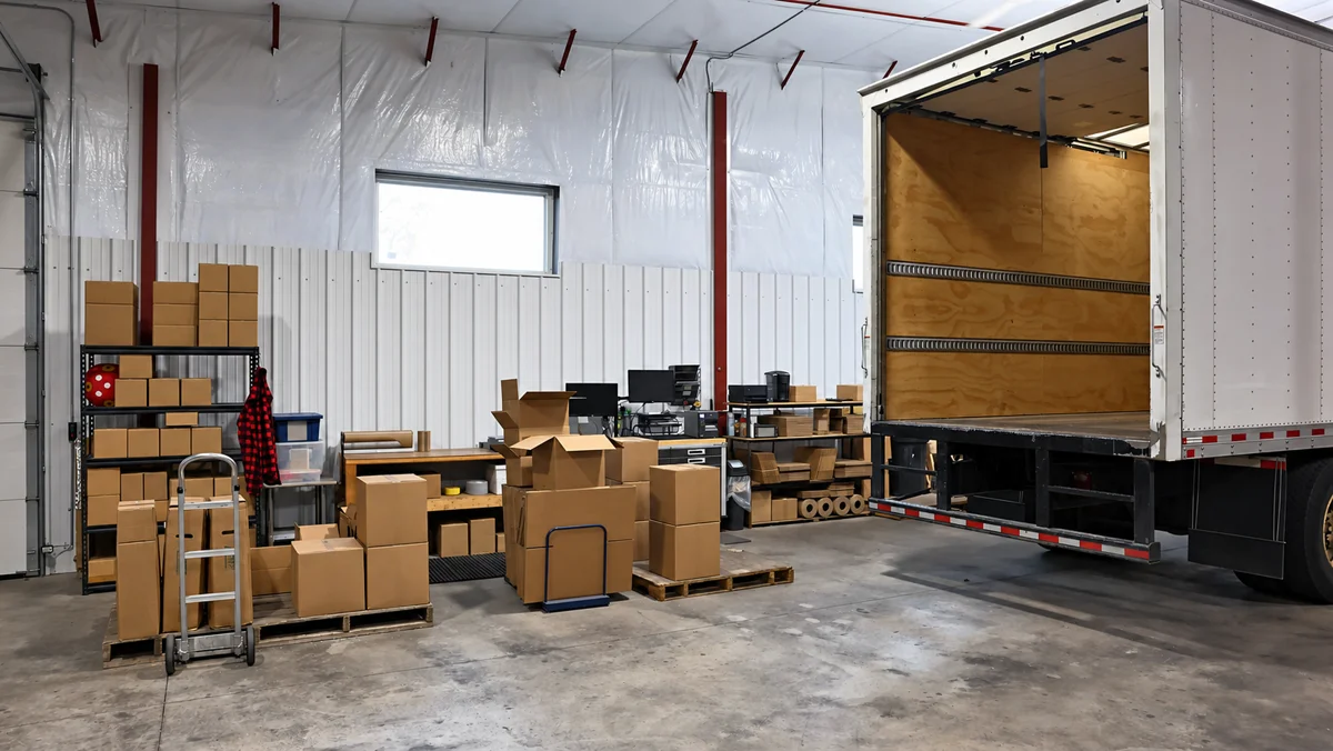 Warehouse interior with stacked cartons on pallets and an open truck trailer at the loading door